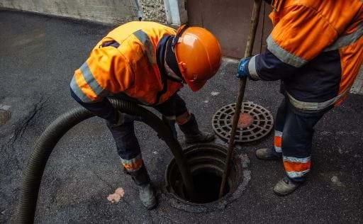 Two Drain Man crew members in safety gear clearing an open drain
