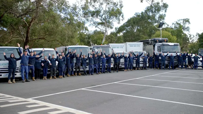 The real Drain Man team waving in front of their fleet